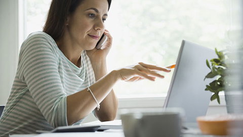 Woman working remotely talking on the phone and pointing to laptop screen.