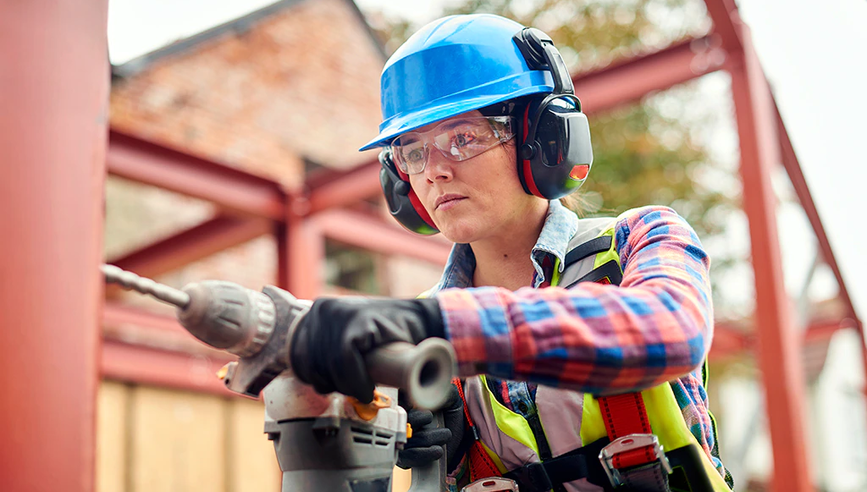 A female construction worker in safety gear drilling on metal.