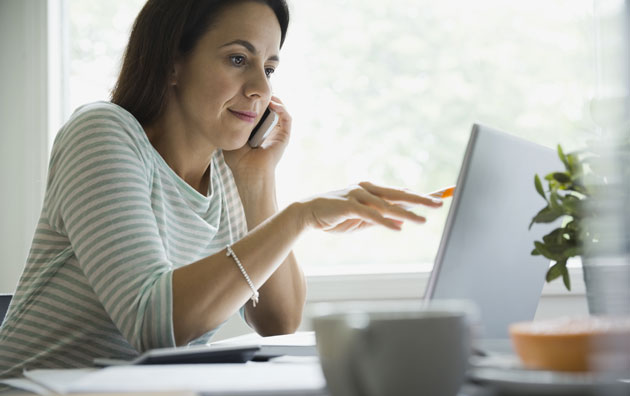 Woman on the cell phone while looking at computer screen.