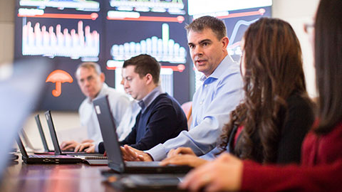 Four people sitting at a desk with laptops.