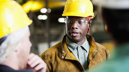 African American man wearing hard hat and glasses meeting with other men.