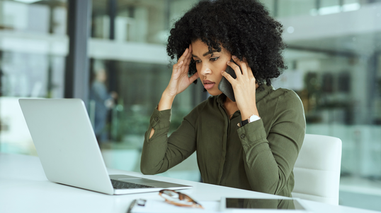 Young, and frustrated African-American woman on the phone while researching on her laptop.