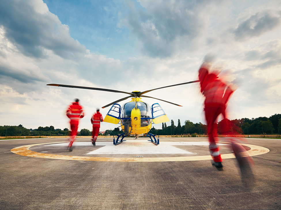 Air ambulance crewmembers run across a helipad toward a waiting helicopter.