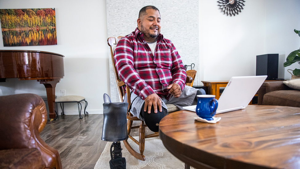 Man with amputated leg sitting at a table with his laptop and a cup of coffee.