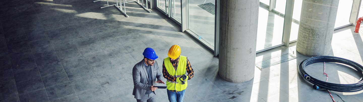 A businessman and construction worker having a meeting onsite and looking at a smart device.