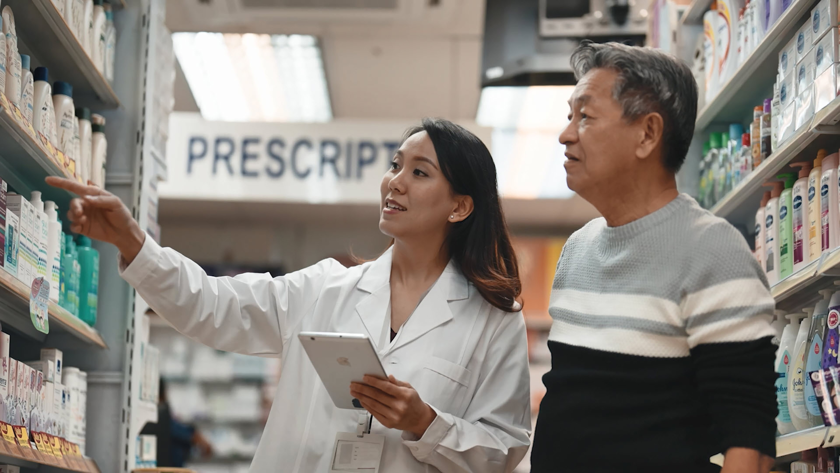 Asian pharmacist looking at shelves with a customer.