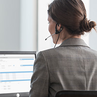 Backside of a female agent wearing a headset helping a customer, sitting in front of a computer screen.