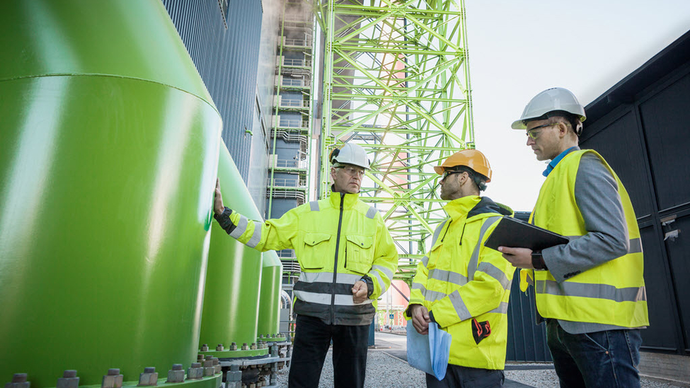 Three men talking outside of a power plant.