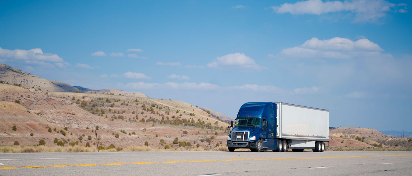 Blue and white semitruck driving on a remote highway road in Arizona under a blue sky.
