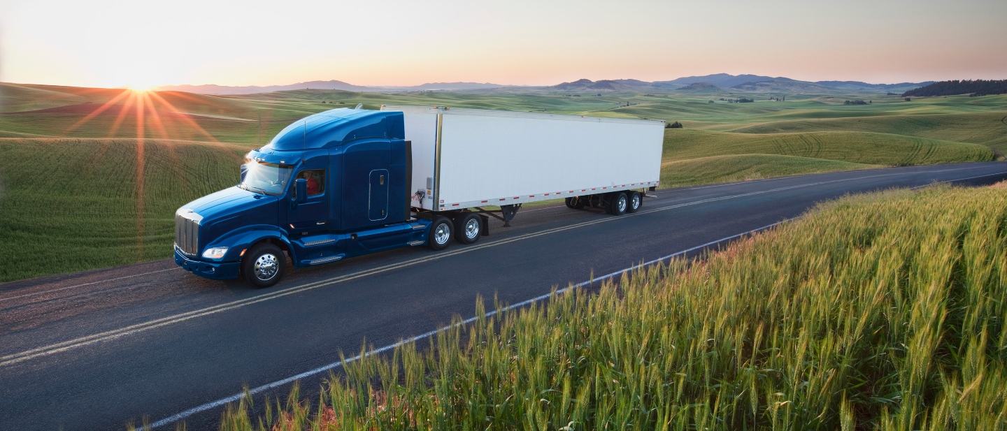 Blue and white truck driving on a remote highway surrounded by fields.