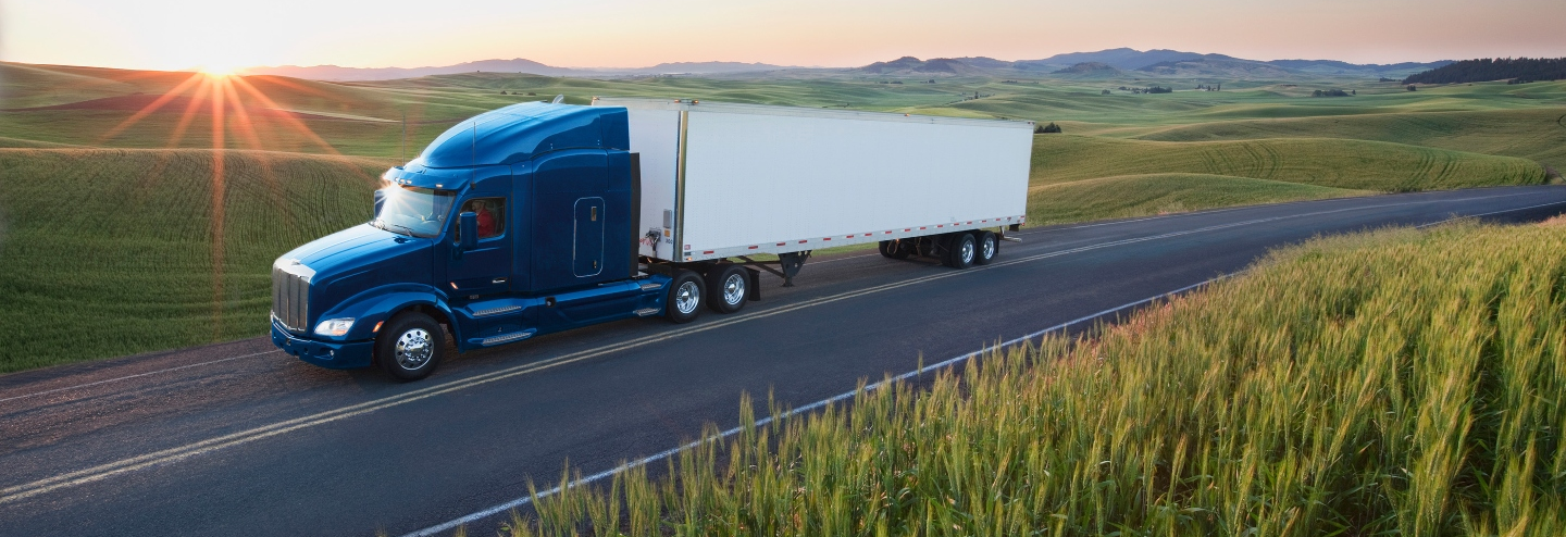 Blue and white truck driving on a remote highway surrounded by fields.