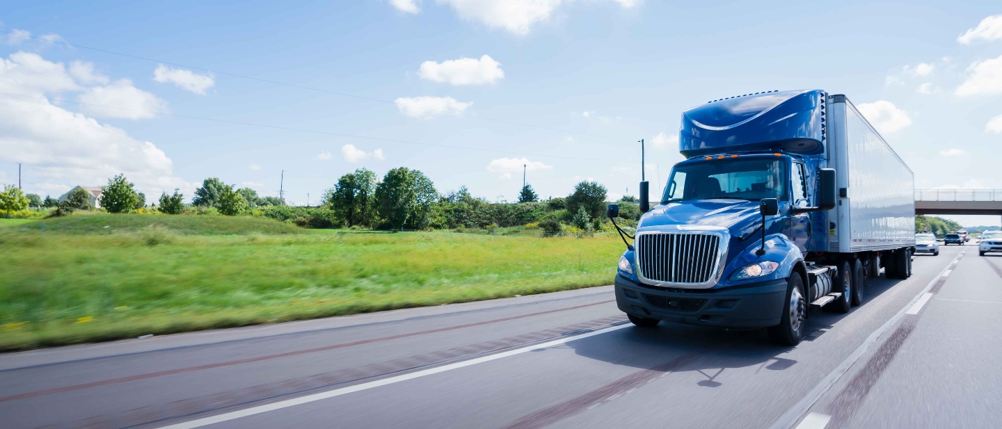 Blue truck delivering goods on the freeway under a blue sky.