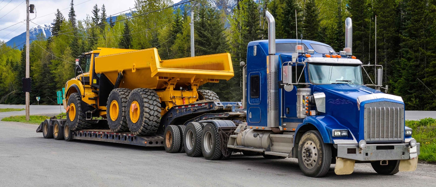 Blue truck hauling a yellow dump truck.