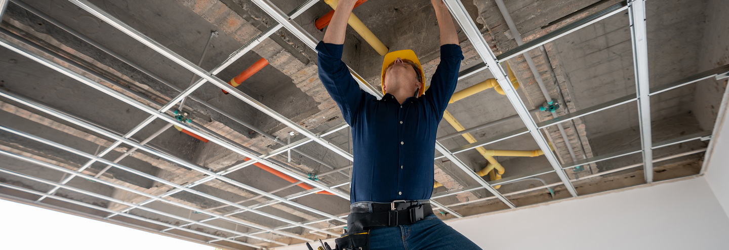 A contractor with plumbing insurance installs a sewer line in the ceiling of new building.