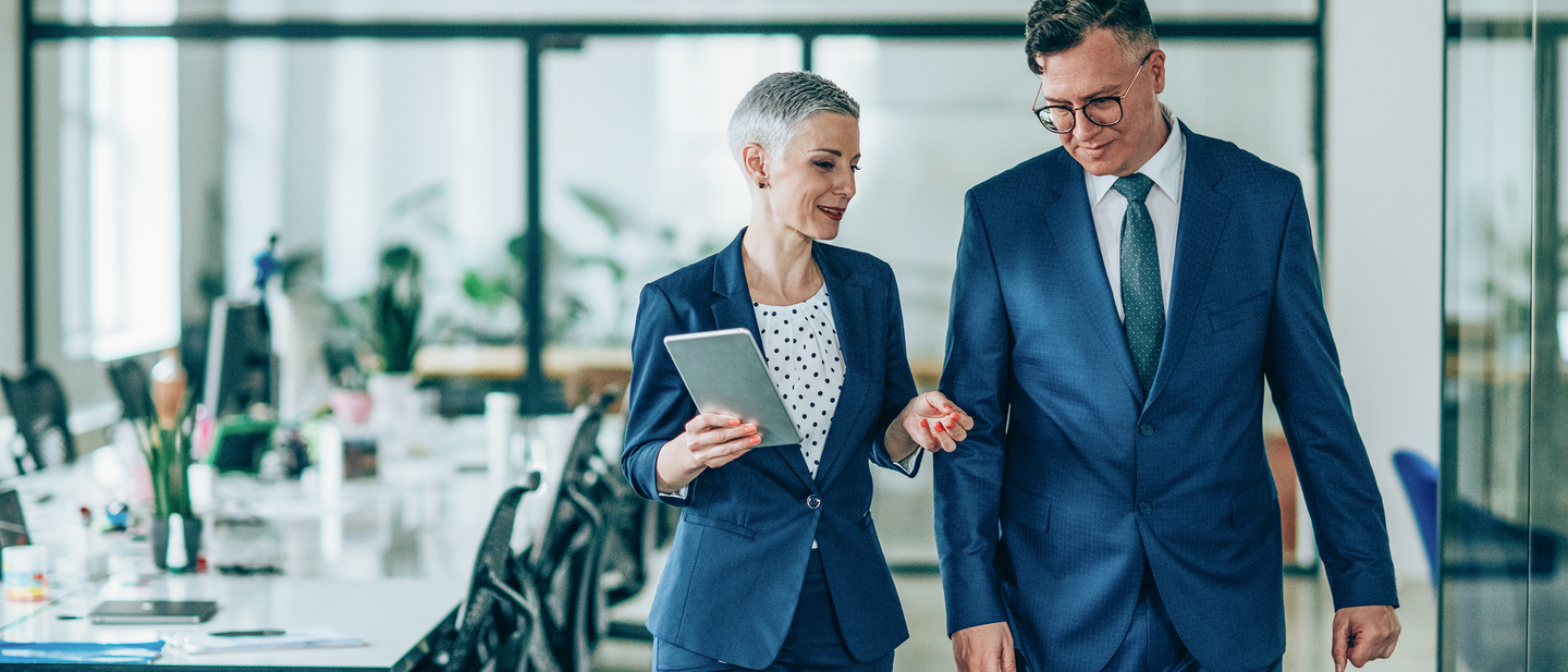 Two professionals walk and talk in a business office.