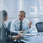 Two professionals discuss business possibilities in tall glass-walled building.