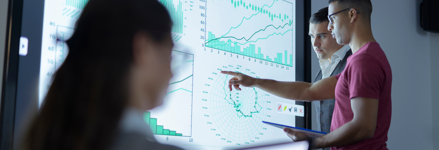 Two men looking at a screen with charts and graphs.