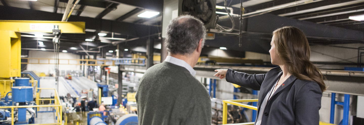 A business man and woman have a discussion in a factory.