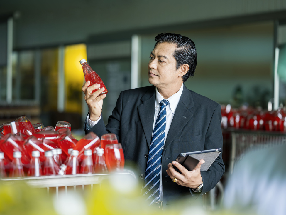 Businessperson looking at fruit flavored drink products in a beverage production facility.