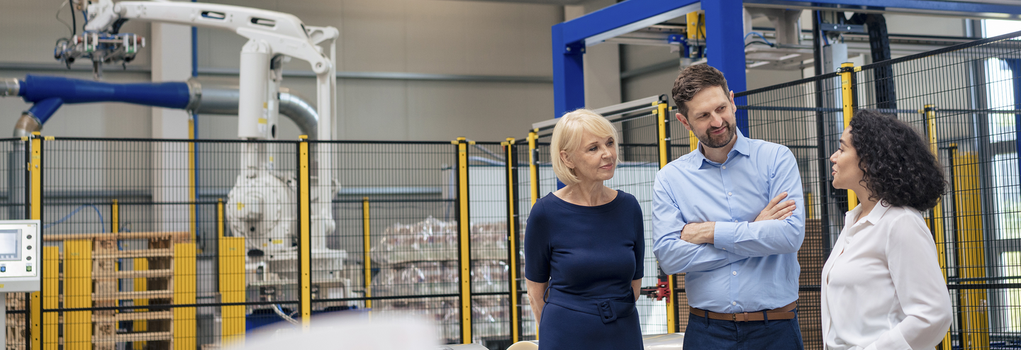 Business managers having a meeting in a warehouse, with machinery in the background.