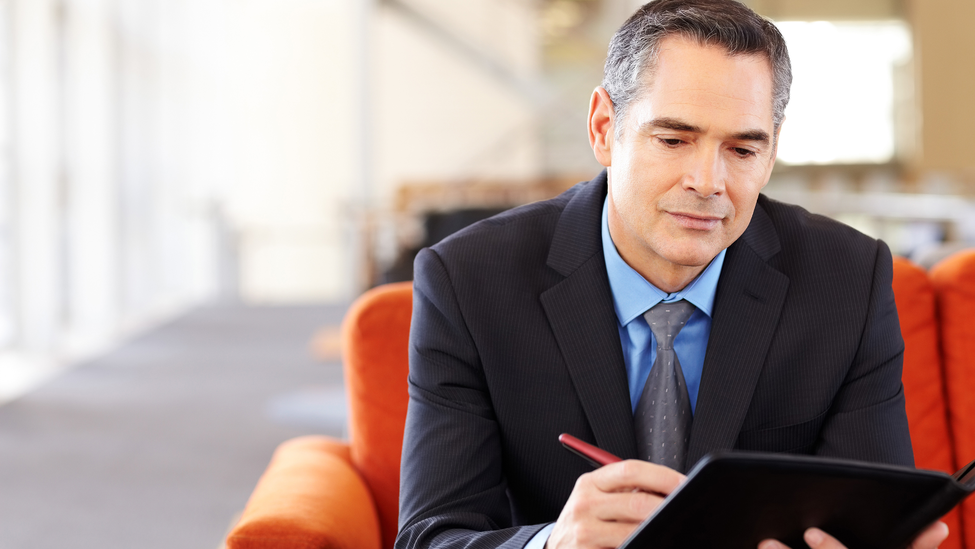 Mature male business manager making notes before meeting while sitting in office lobby. Horizontal shot.; Business Manager Making Notes Before Meeting