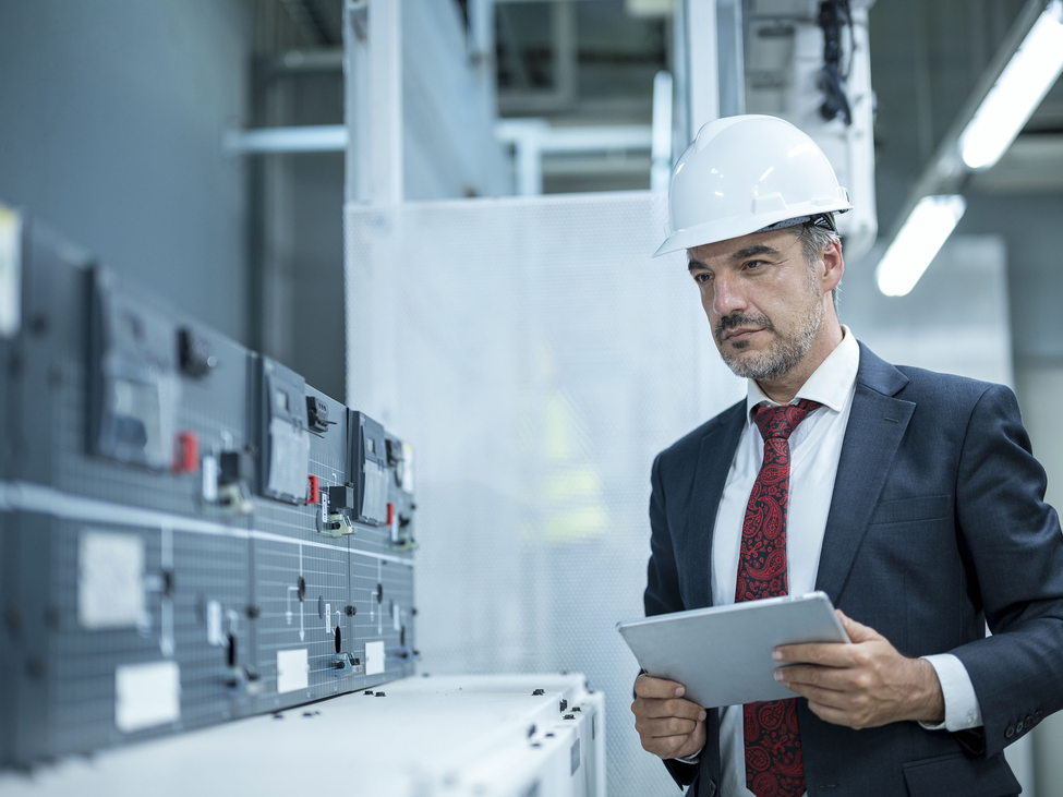 Businessman with tablet in electricity control room of a factory.