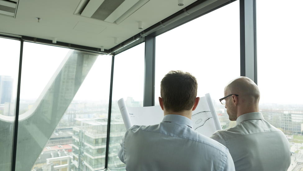 Two businessmen in office looking at blueprint.