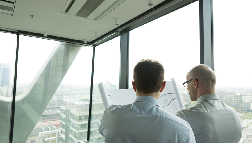 Two businessmen in office looking at blueprint.