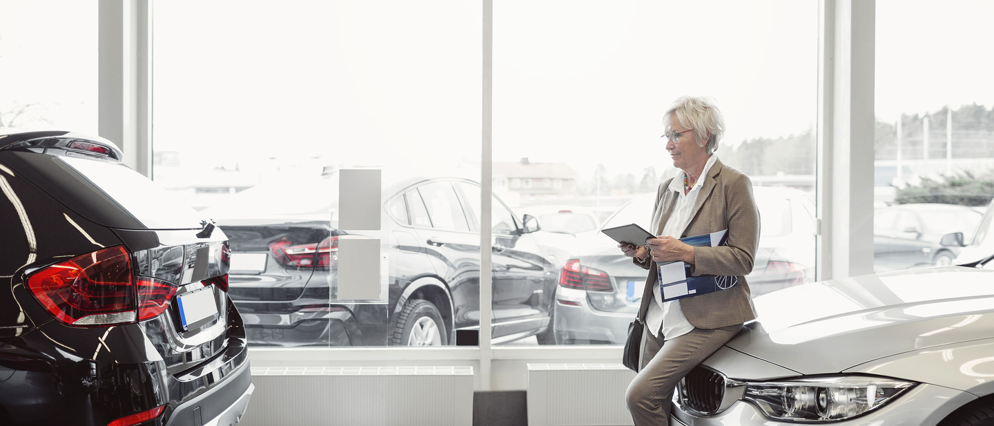 Auto dealer leans on a car for sale on a showroom floor. 