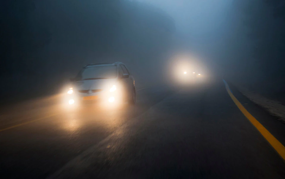 Car driving in fog at night with headlights on.