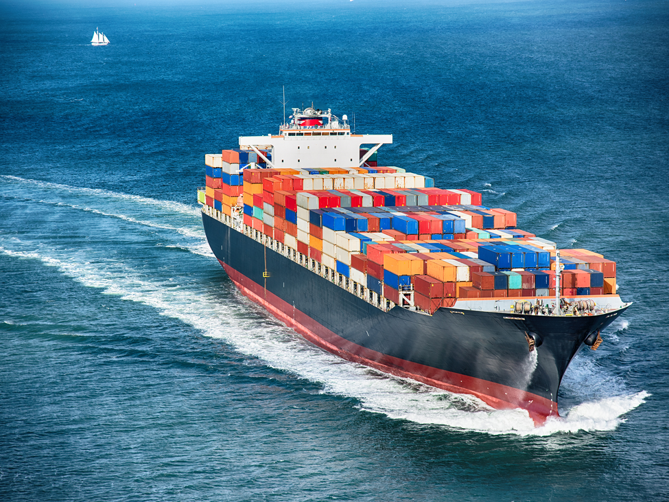 A large cargo ship loaded with shipping containers makes a wide turn mid-ocean.