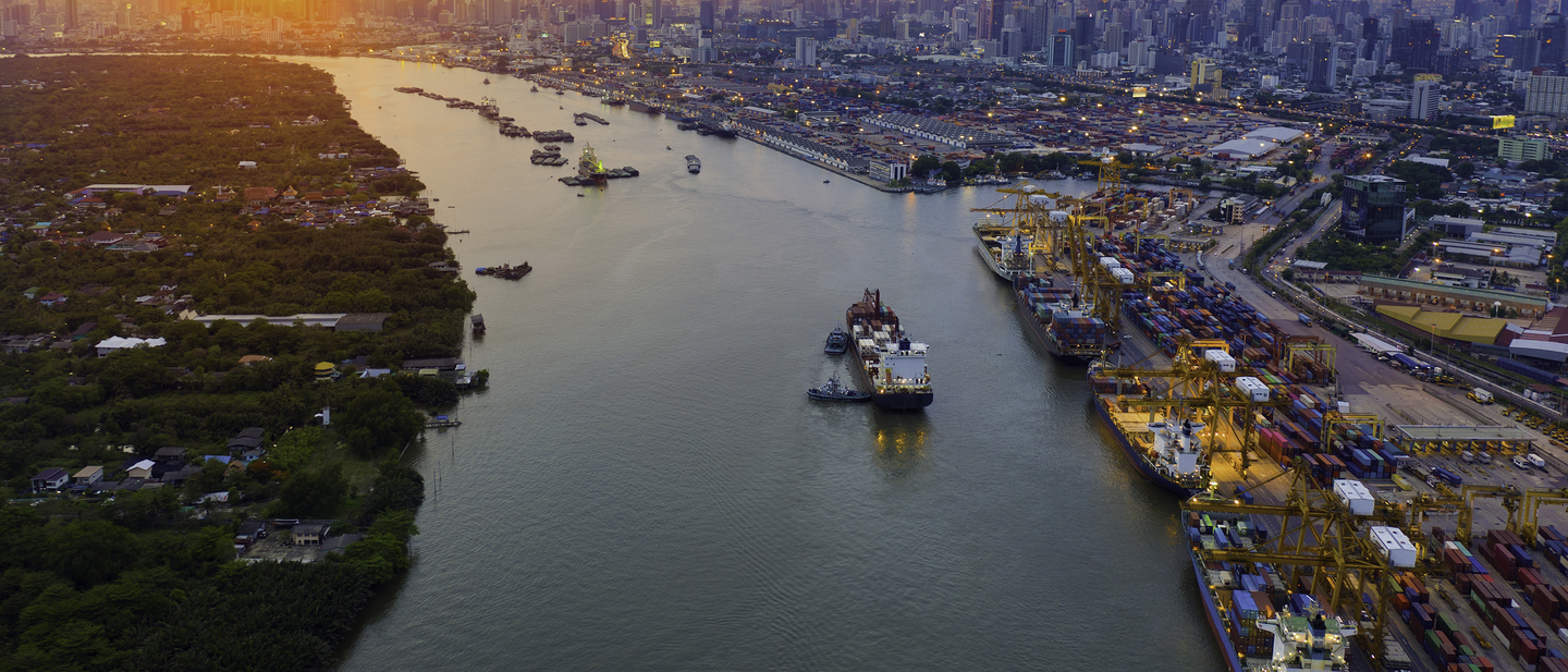 Cargo ships moving goods in a supply chain along a river at sunset.