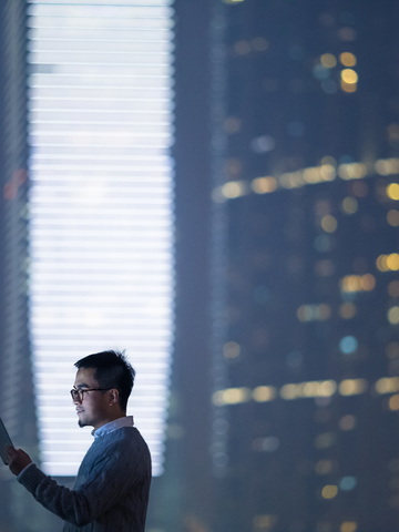 Businessperson looks at mobile device in front of an office building at twilight.