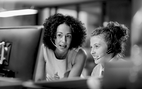 Employees in a call center wearing heat sets and talking with someone in front of a computer