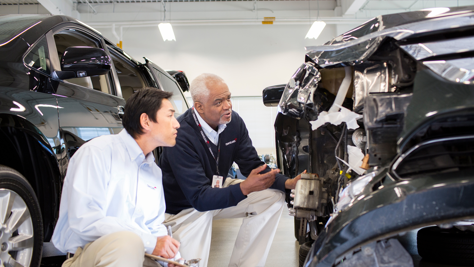 Two men crouching to examine a car that has been in an accident.