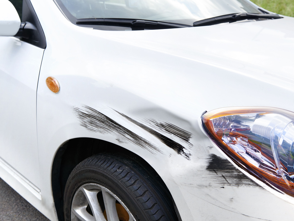 Three-quarter view of front passenger side of a white sedan showing collision damage.