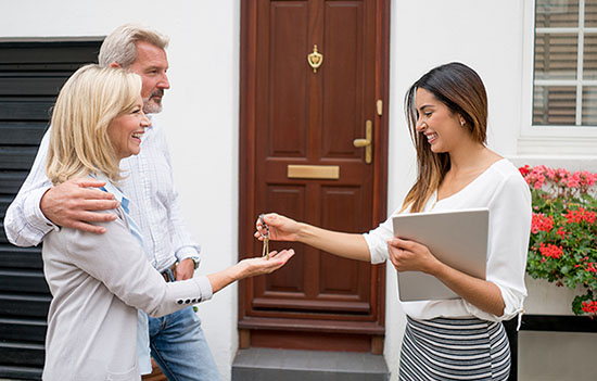 Happy new homeowners in front of their new house, with a real estate agent handing them the keys.