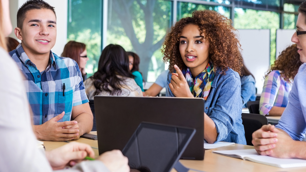 Group of young people sitting at table with laptops.