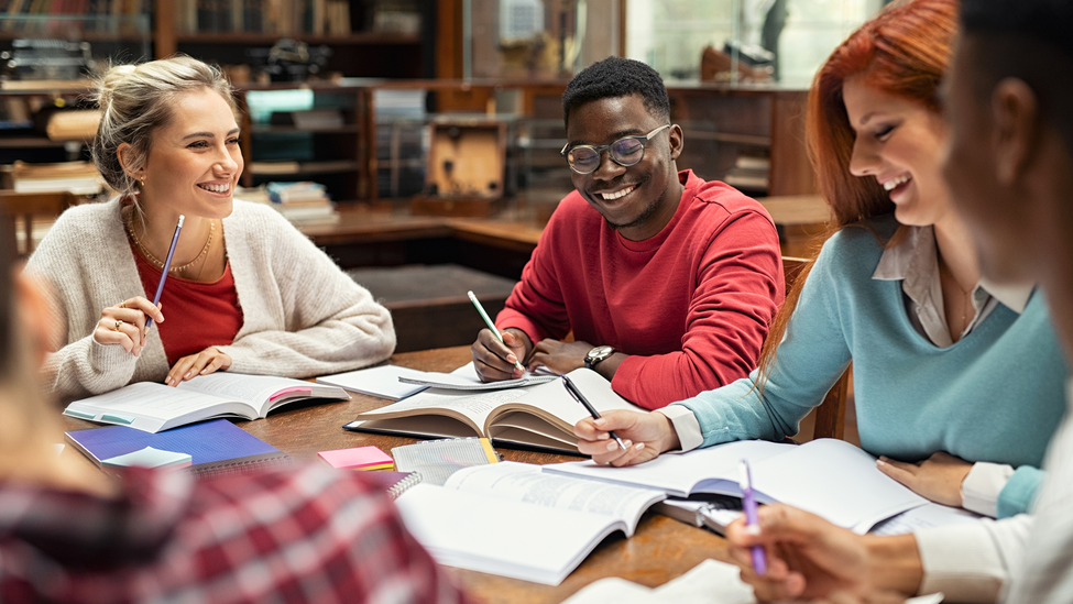 A group of people studying with open books at a desk.