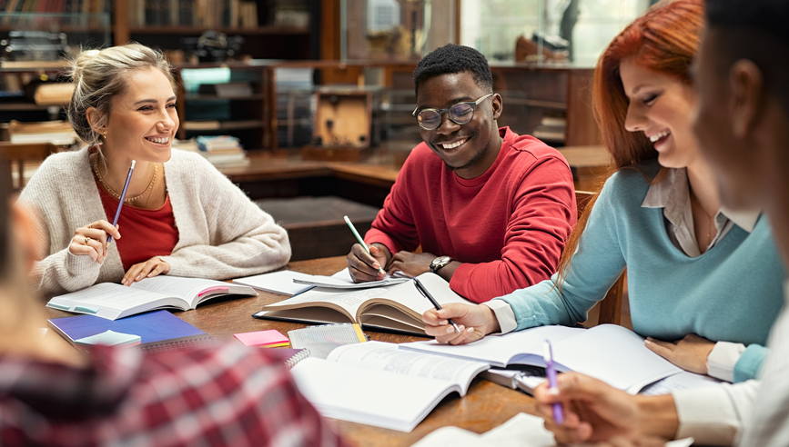 A group of people studying with open books at a desk.