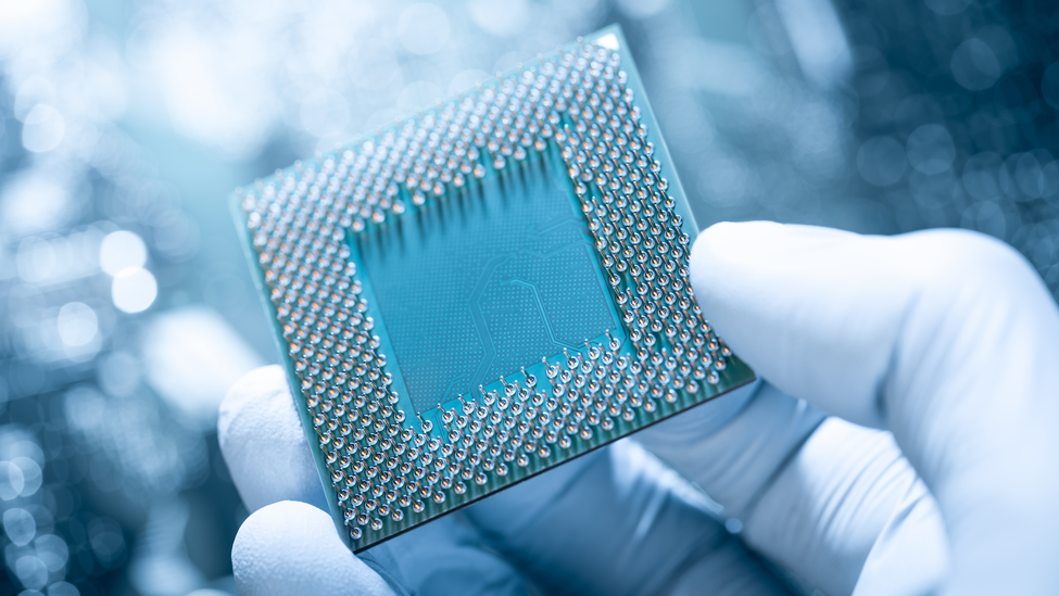 Electronic technician with gloves holding chip. Circuit board in background.