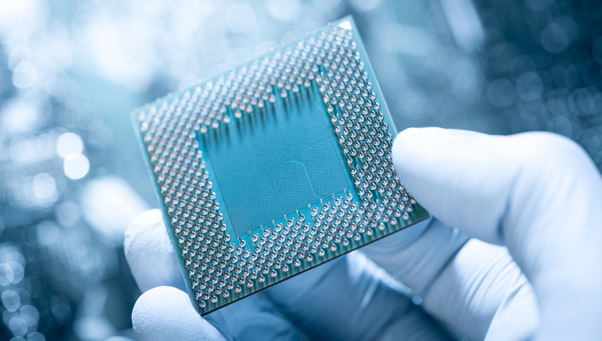 Electronic technician with gloves holding chip. Circuit board in background.