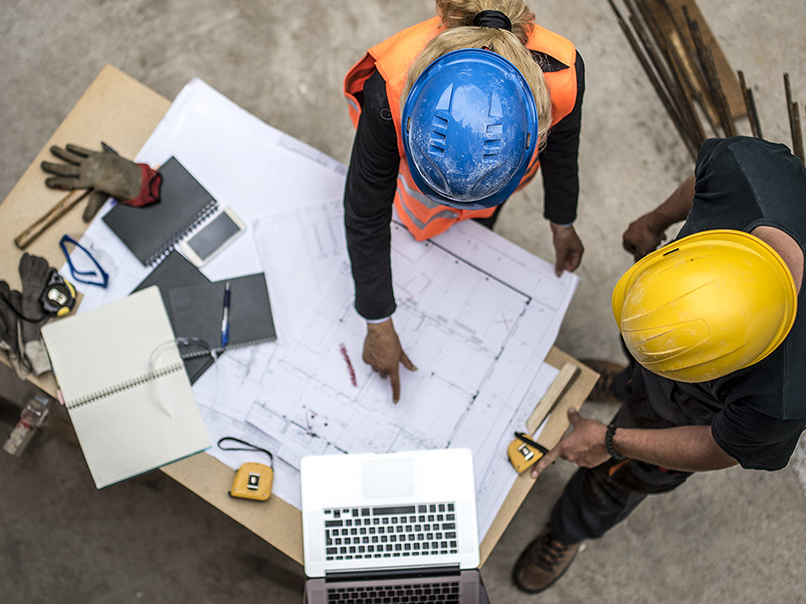 overhead view of two construction site managers or workers studying blueprints