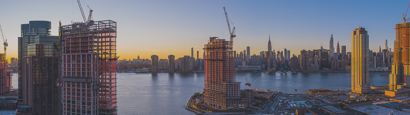 View of skyscrapers being built at sunset along a waterfront.