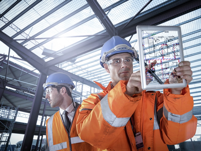 Two male construction workers on site inspecting and one of them touching a tablet.