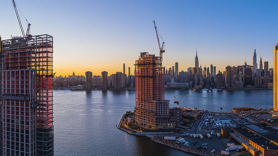 View of skyscrapers being built at sunset along a waterfront.
