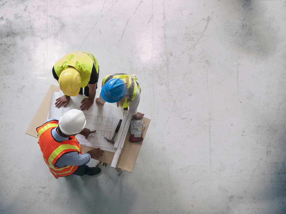 Overhead view of three professionals looking at blueprints in an empty building.