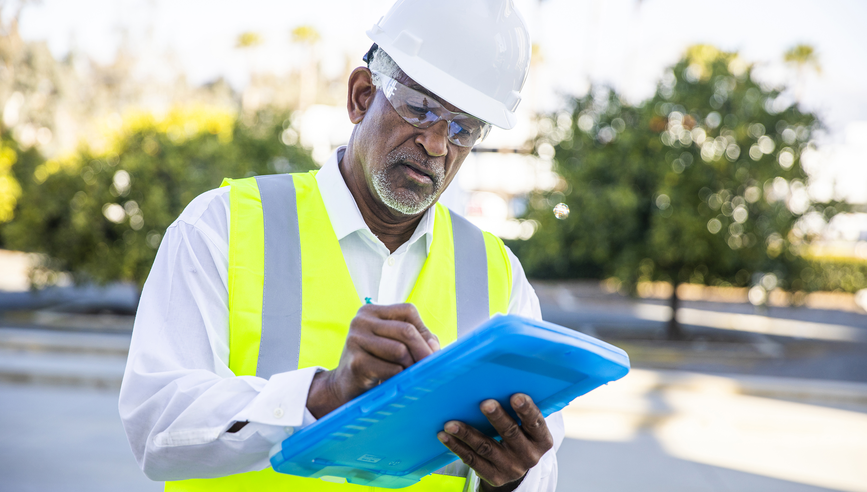 Construction worker holding a clipboard looking over paperwork.