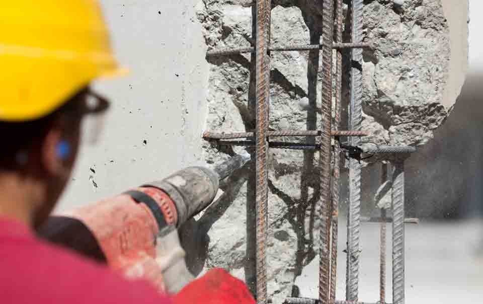 Construction worker drilling into concrete wall.