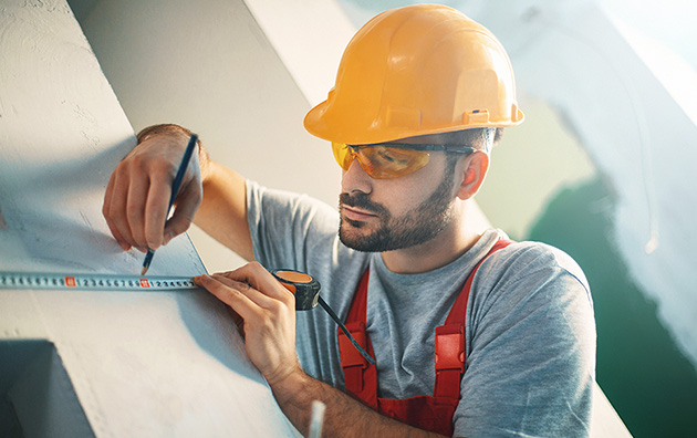 Contractor in a yellow hard hat measuring a wall.